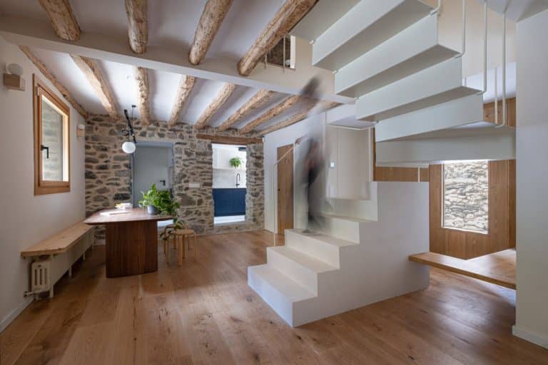 Salón con vigas de madera, escalera blanca y comedor