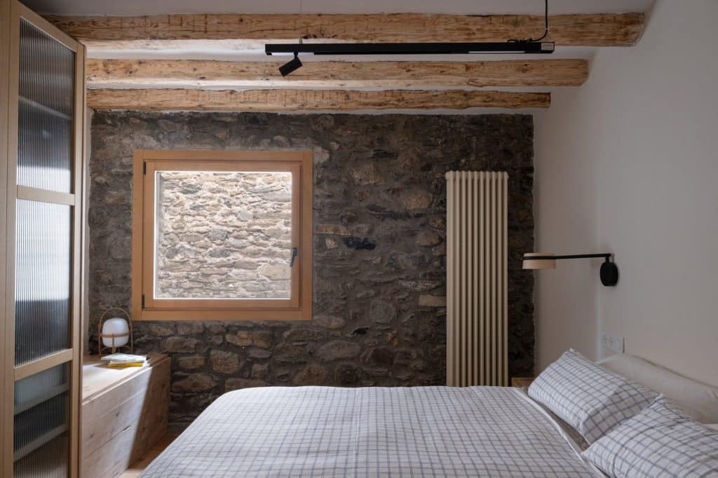 Dormitorio con muro de piedra vista y vigas de madera
