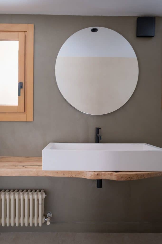 Baño con lavabo sobre encimera de madera y espejo redondo