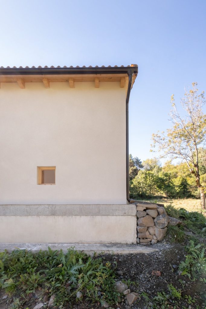 Esquina del edificio con alero de madera y muro de piedra en San Feliu de Veri