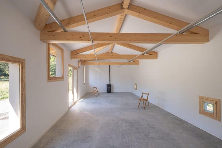 Sala expositiva con cerchas de madera vistas y losa de hormigón