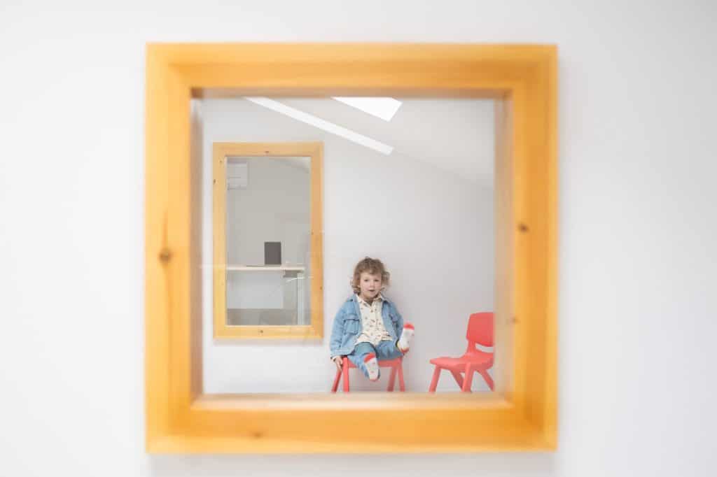 Hueco interior enmarcado en madera con una niña sentada en una silla roja