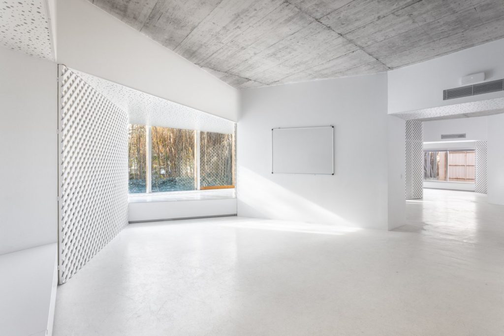 Sala con forjado de hormigón visto, celosía blanca y pizarra