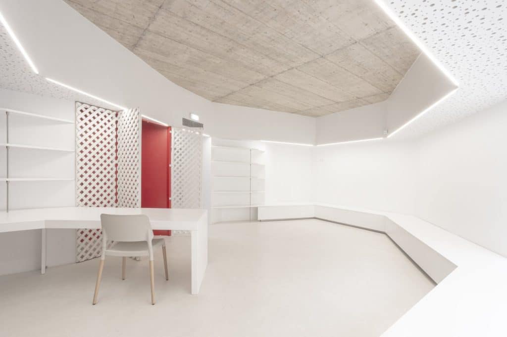 Sala con mesa, estanterías y puerta roja entre celosías blancas