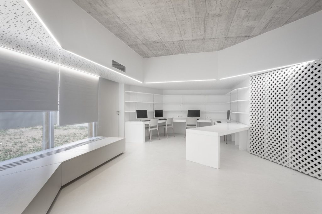 Sala de ordenadores con mesas blancas, banco corrido y celosía