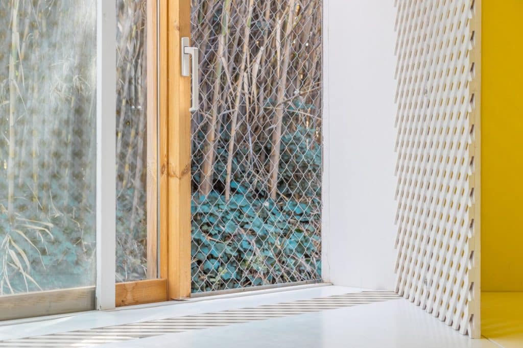 Detalle de ventana de madera con malla metálica y celosía