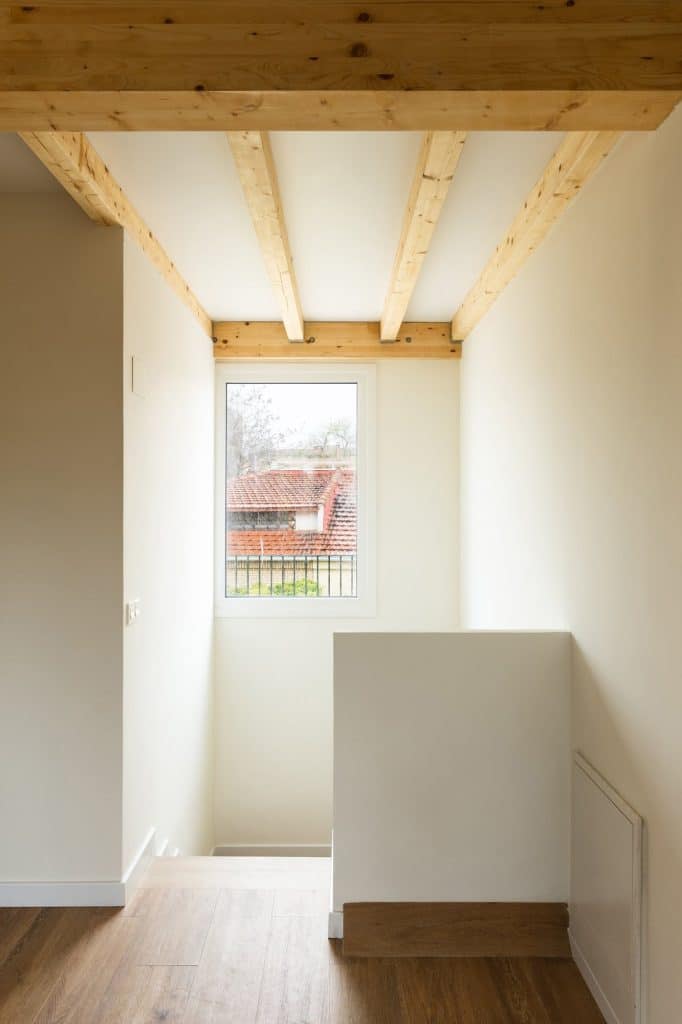 Hueco de escalera con vigas de madera y ventana a las cubiertas del barrio